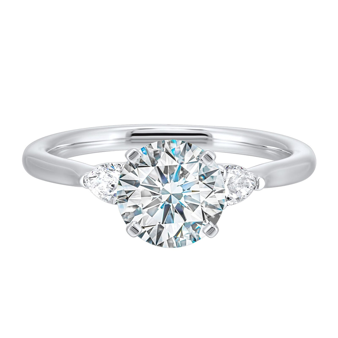 Stunning engagement ring features a round brilliant cut diamond in the center of a three stone setting, adorned on either side by a smaller pear diamond set on the tapered shank.