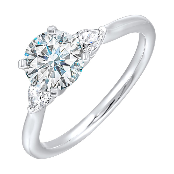 Stunning engagement ring features a round brilliant cut diamond in the center of a three stone setting, adorned on either side by a smaller pear diamond set on the tapered shank.