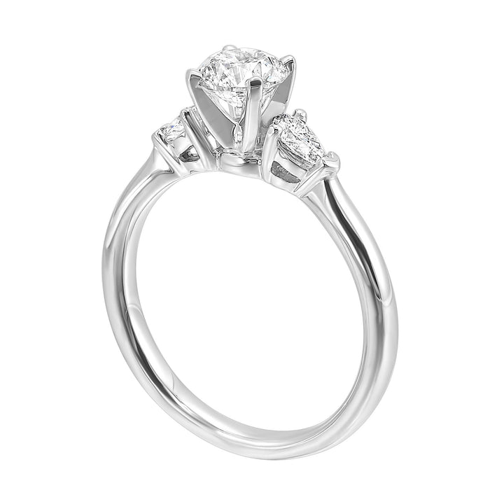 Stunning engagement ring features a round brilliant cut diamond in the center of a three stone setting, adorned on either side by a smaller pear diamond set on the tapered shank.