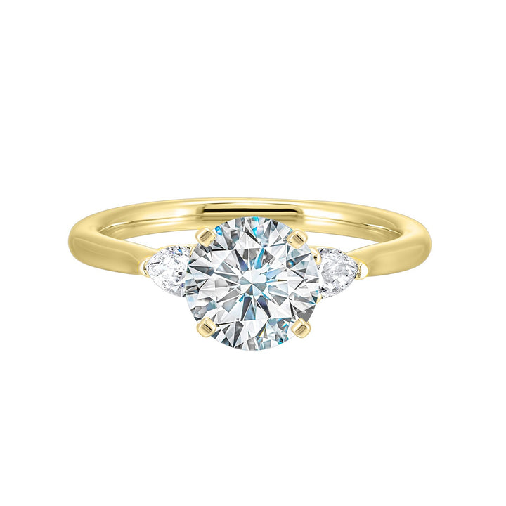 Stunning engagement ring features a round brilliant cut diamond in the center of a three stone setting, adorned on either side by a smaller pear diamond set on the tapered shank.