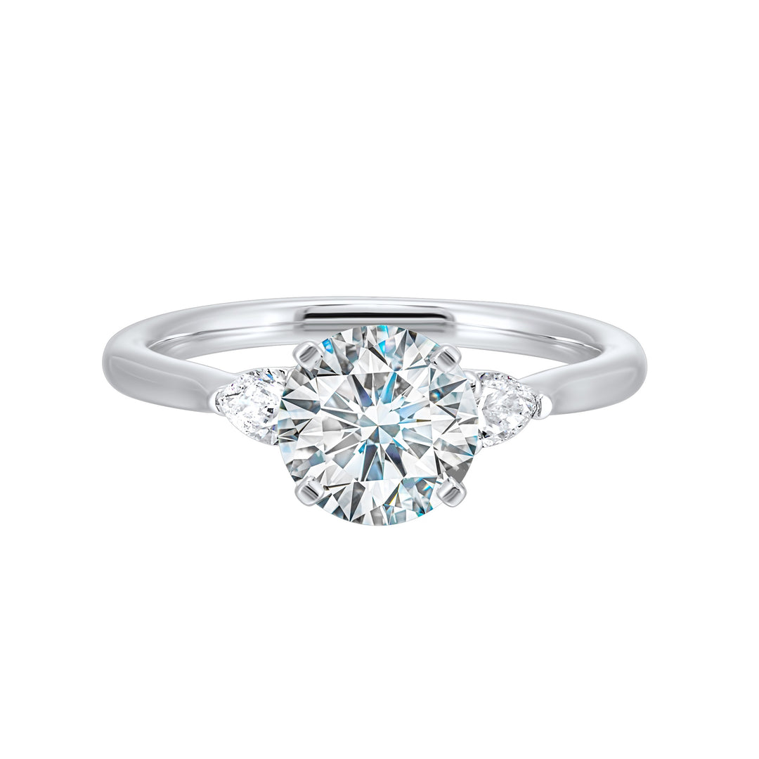 Stunning engagement ring features a round brilliant cut diamond in the center of a three stone setting, adorned on either side by a smaller pear diamond set on the tapered shank.