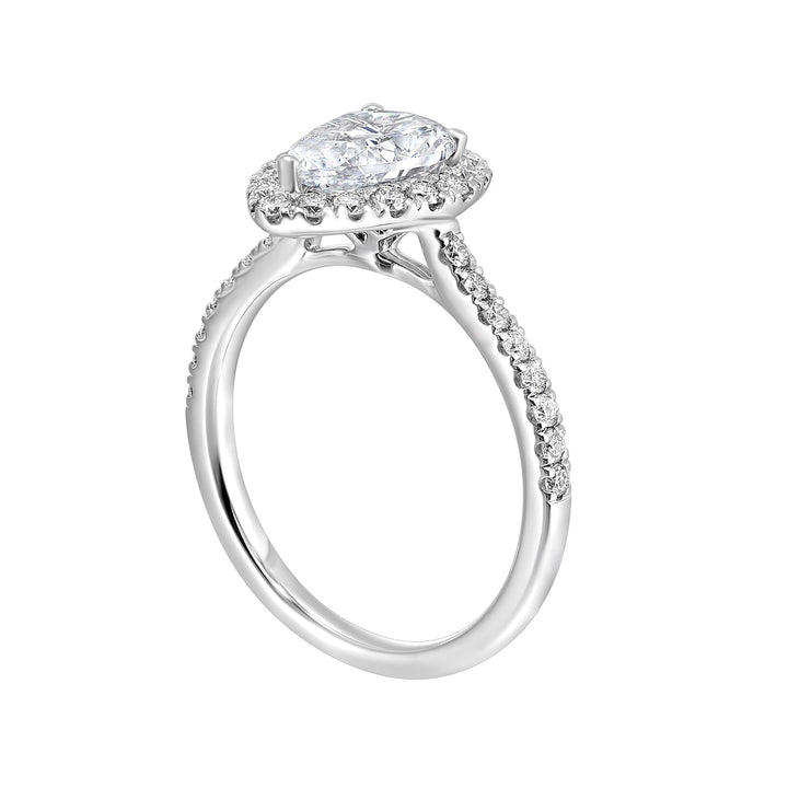 The pear cut solitare shines in this elegant ring, embraced by a delicate halo. The diamond shank adds a touch of sparkle, showcasing the beauty of the pear and halo at its finest.